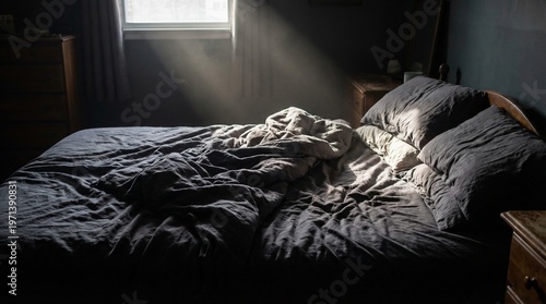 Foto A moody shot of an unmade bed with dark grey sheets, hit by a strong shaft of light from a window