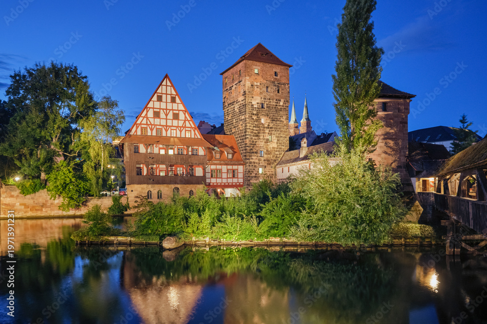 Naklejka premium Night view of the illuminated Weinstadel and medieval towers reflecting in the Pegnitz river in Nuremberg, Bavaria, Germany.