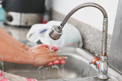 A person washing their hands under a kitchen faucet.