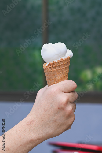 A hand holding a vanilla ice cream cone.