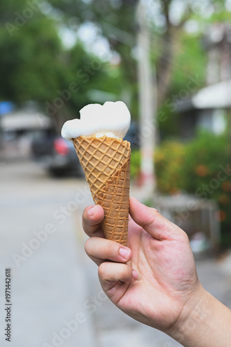 A hand holding a vanilla ice cream cone.