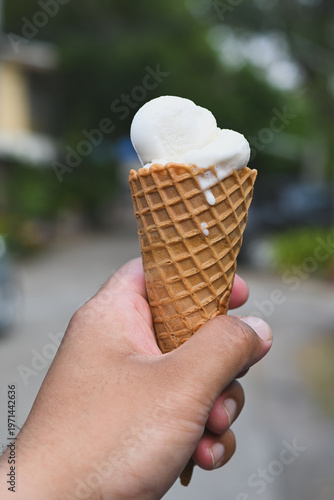 A hand holding a vanilla ice cream cone.