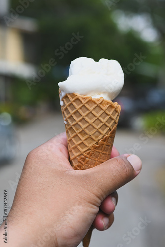 A hand holding a vanilla ice cream cone.