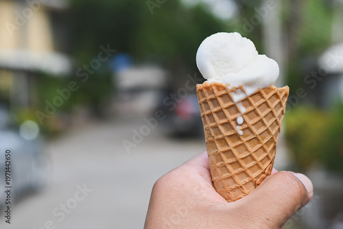 A hand holding a vanilla ice cream cone.