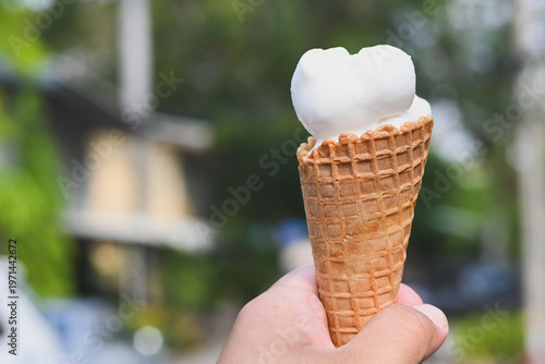 A hand holding a vanilla ice cream cone.