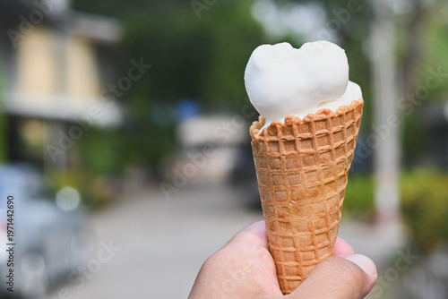A hand holding a vanilla ice cream cone.