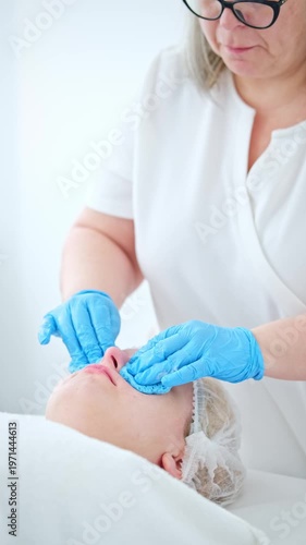 A beautician applies lotion to a woman's face while performing a massage during her facial cleansing treatment. This session takes place in a spa setting with a focus on skincare.