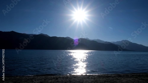 Cinematic shot of Pangong Lake during early morning, with soft golden light reflecting on the calm water as birds gently glide across the surface. Ideal moment for travel and nature storytelling.