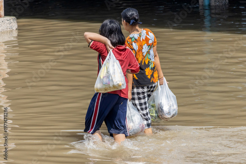 A woman and a girl wade with bags through a flooded street, Thailand