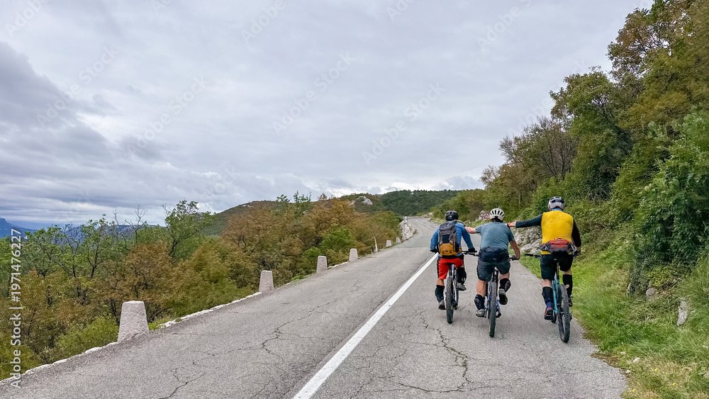 Obraz premium Three friends cycling together on a mountain road surrounded by trees and overcast sky