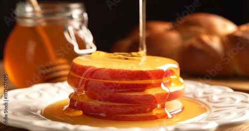 Sliced apples drizzled with honey on a decorative plate, with a jar of honey and bread in the background