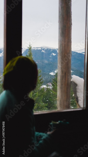 woman looking out the window at a beautiful landscape, snowy mountains and forest, winter