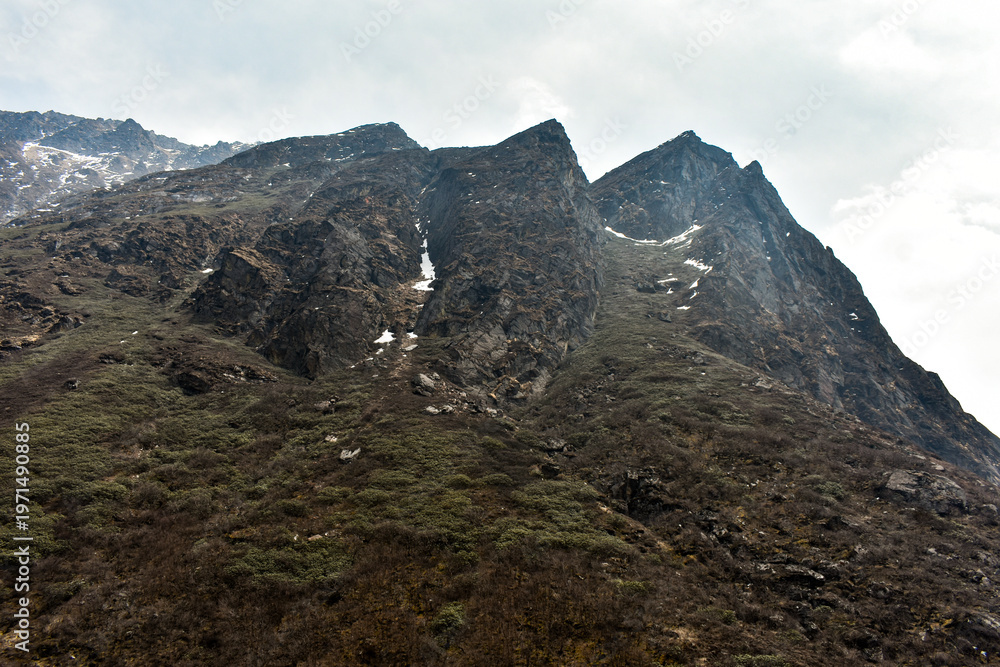 Fototapeta premium Rugged Himalayan mountain peaks with snow patches under cloudy sky, showcasing dramatic high altitude landscape in North Sikkim.