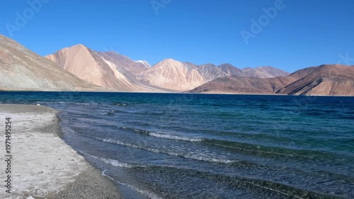 Cinematic shot of Pangong Lake during early morning, with soft golden light reflecting on the calm water as birds gently glide across the surface. Ideal moment for travel and nature storytelling.