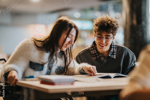 Cuadro en lienzo Two students sit side by side reading and discussing a book while smiling