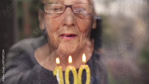 Portrait of an elderly woman with glasses holding anniversary candles.  An old woman holds a birthday cake alone on her centenary.