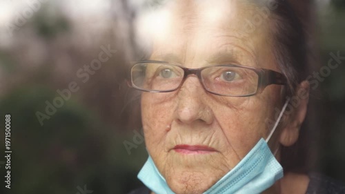 Portrait of an elderly woman in a window after quarantine with her mask removed. An old woman in a window with her mask down, after the pandemic.