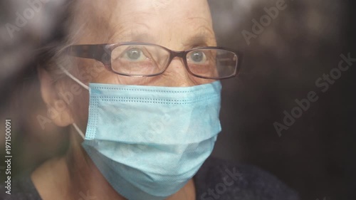 Portrait of an elderly woman in a window after quarantine with her mask removed. An old woman in a window with her mask down, after the pandemic.