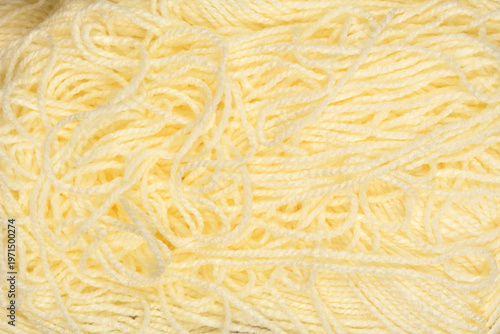 A detailed close up view shows the soft and twisted fibers of a messy pile of light yellow wool knitting yarn