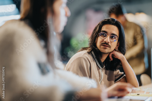 Foto A young student with glasses attentively listens to a coworker during an informal office conversation