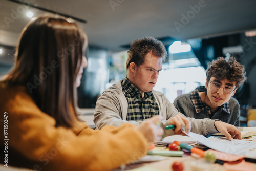 A group of young students studying together at a table, collaborating on papers and supplies. The scene shows focused, inclusive learning and peer support during a study session.