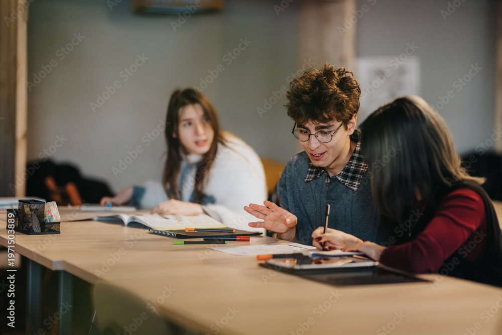 Fototapeta premium Three students study and discuss papers and notes at a long table. A small study group collaborates and shares ideas while working on assignments.