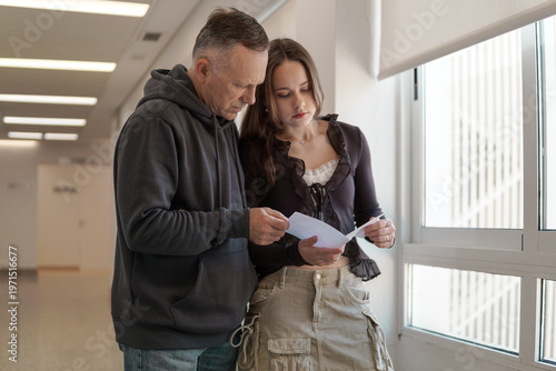 Father and daughter discussing documents in hospital lobby. Doctor consultation or administrative paperwork scene. Family support and legal advice in modern clinic.
