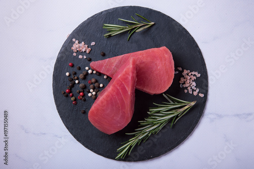 Raw fresh tuna steaks on a black stone board against a light marble background. Side view.