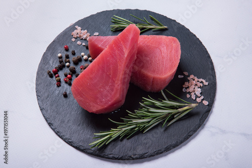 Raw fresh tuna steaks on a black stone board against a light marble background. Side view.