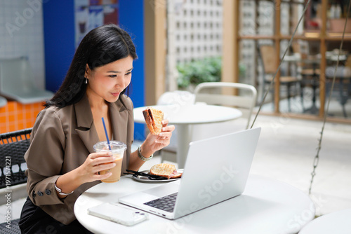 Foto Beautiful Asian businesswoman eating breakfast in a cafe with a sandwich and cof