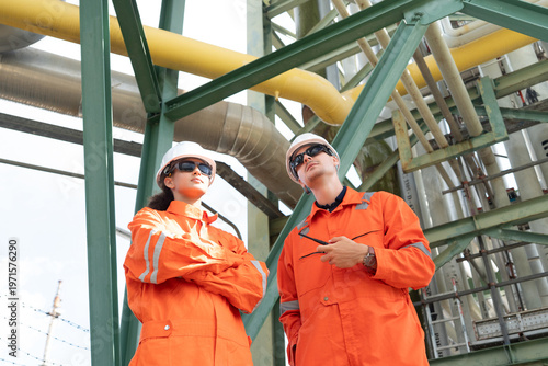 Photos Two Workers Inspect Yellow Pipe in Bright Industrial Refinery Setting with Prote