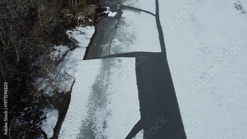Frozen river with cracks under sunlight near forest in winter season