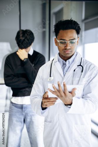 Doctor in white lab coat examining digital medical records on a tablet, consulting patient information in a clinic