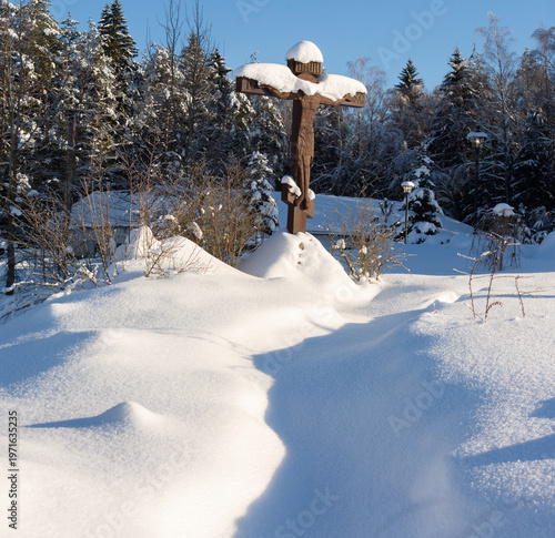 A cross standing firmly at the top of a snowy hill in the forest
