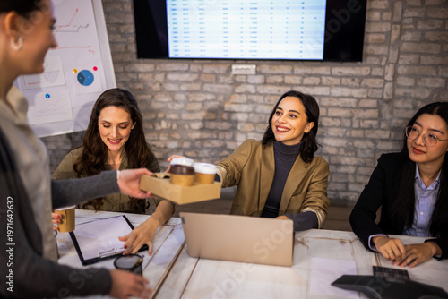 Fotografie Kind female colleague bringing coffee to coworkers working at their desks in a modern office