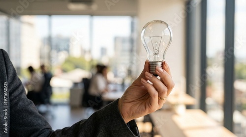 Close up hand holding clear light bulb in bright office with city view