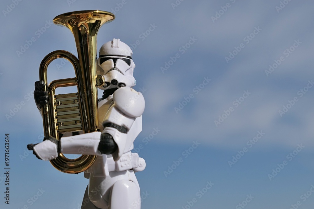Fototapeta premium Action figure of Star Wars clone trooper in white helmet and armor holding model of some kind of euphonium brass instrument, blue spring skies with overcast clouds in background. 