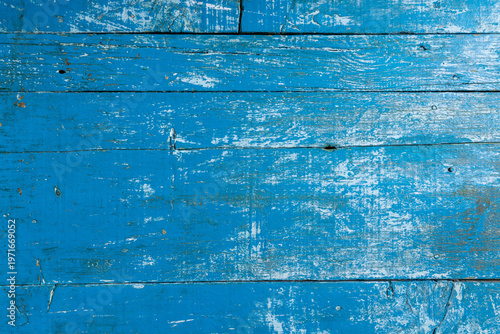 Close-up of weathered blue painted wooden planks with peeling layers, cracks and aged texture. Rustic surface ideal for vintage backgrounds and design use.