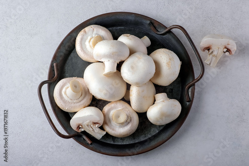 Top view of fresh white button mushrooms neatly arranged in a rustic iron pan on a light background. Perfect for cooking, recipes, or culinary-themed projects and ideas.
