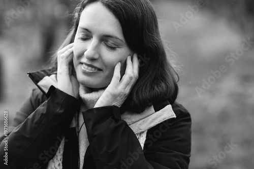 Pretty caucasian woman in her 40s with dark hair wearing warm clothes listening to music outdoors using earbuds and phone. Mature female enjoying her personal time, dancing and breathing fresh air.
