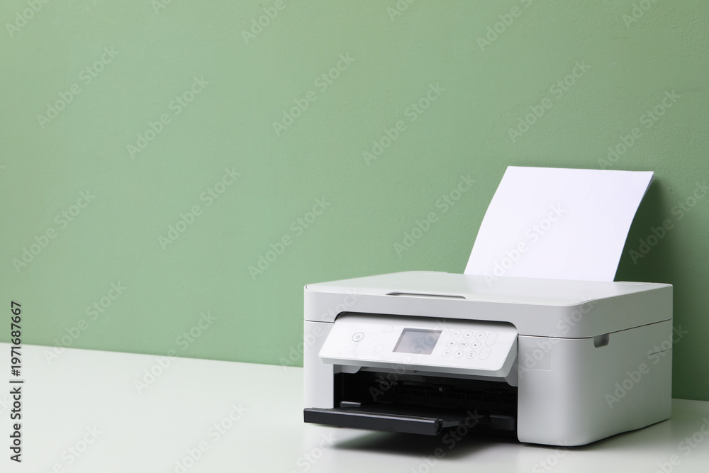 Fototapeta premium One printer with sheet of paper on white table near green wall, closeup. Space for text