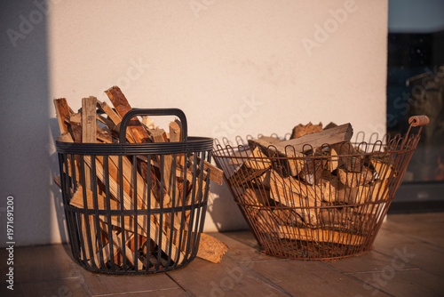 Foto Two decorative metal baskets filled with dry chopped firewood standing on a patio