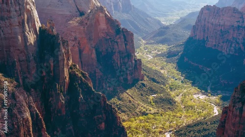 aerial view looking down into Zion Canyon from the Observation Point viewpoint, accessible via the East Mesa Trail. The footage captures the iconic steep red cliffs, a winding river (Virgin River), an