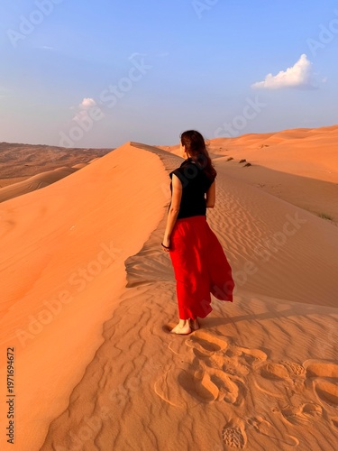 фотографія Woman seen from behind in the Omani desert, standing at the top of a sand dune -