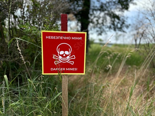 Foto Warning sign with skull symbol and text “Danger Mines!” marking a dangerous area in a forest landscape in Ukraine