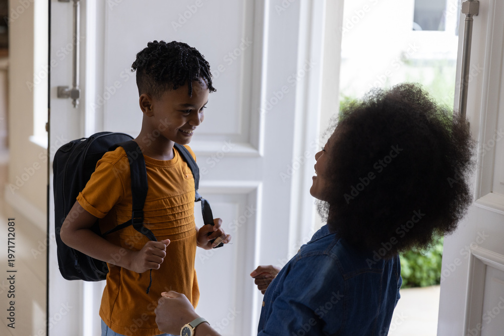 Obraz premium Mother and son smiling and talking at front door, boy wearing backpack and orange T-shirt
