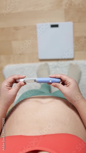 A vertical close up of an young woman giving an injection to her belly
A young woman giving an injection of semaglutide to her belly on floor and scales background