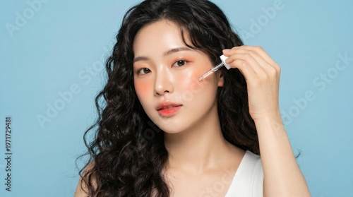Young asian beauty woman curly long hair with korean makeup style on face and perfect clean skin using dropper serum on isolated blue background