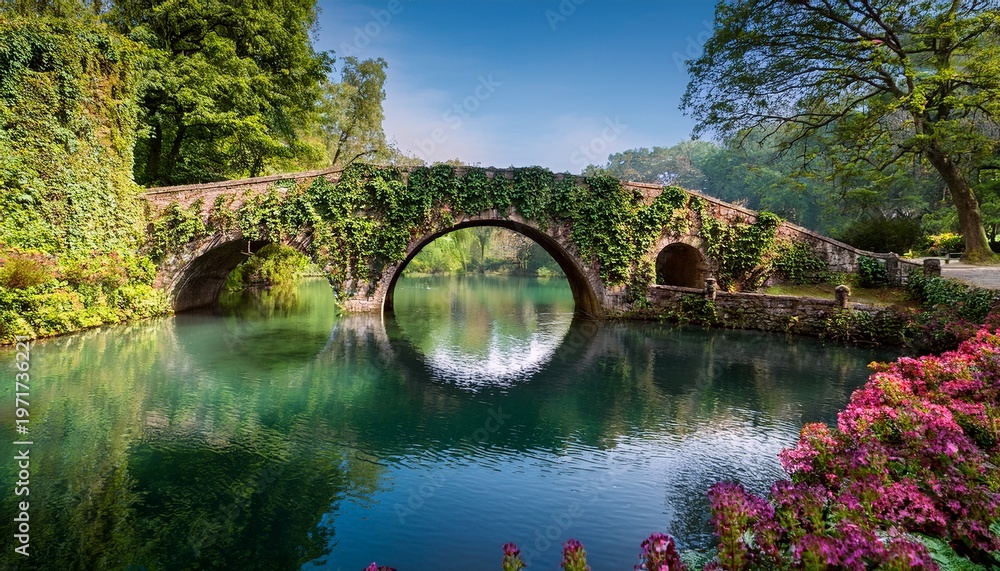 Fototapeta premium overgrown with vines and flowers a historic stone bridge spans a serene lake in the gardens of ninfa latina italy bridge