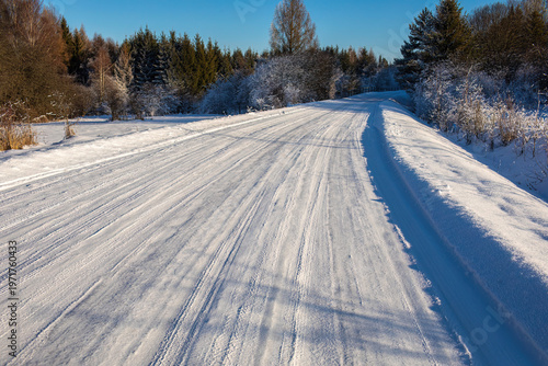 Sunny icy winter road with dangerous slippery surface and tire tracks